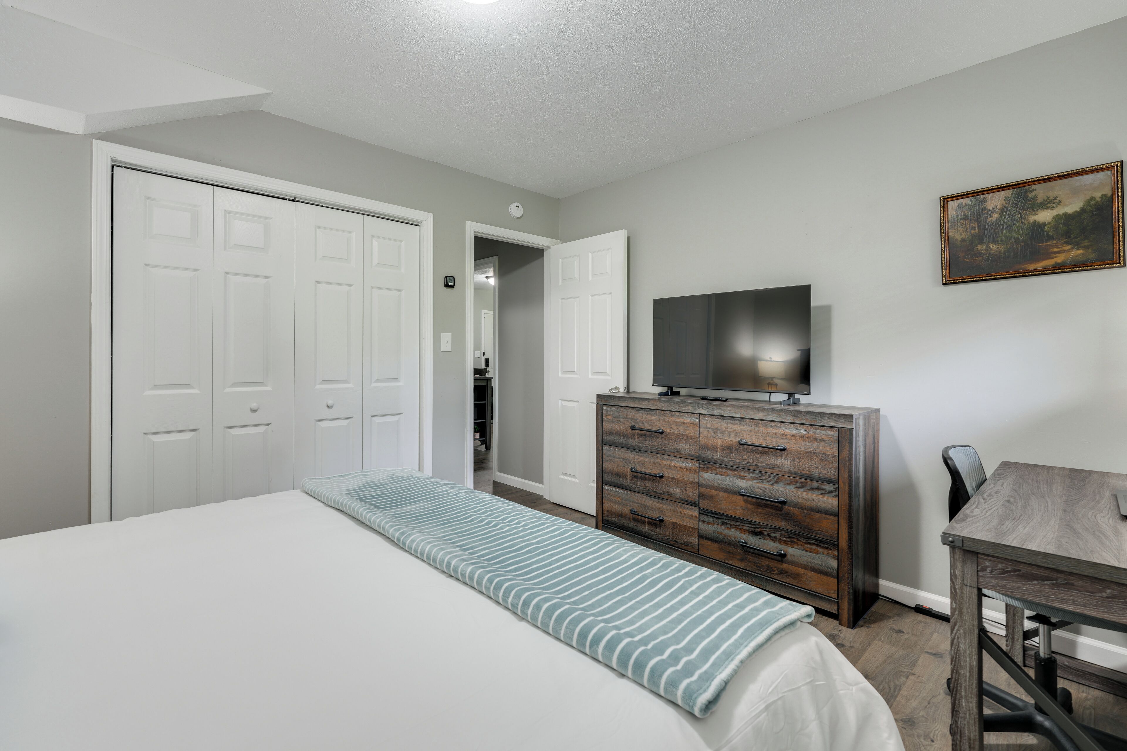 A bedroom with a bed, a dresser, a television, and a painting on the wall.