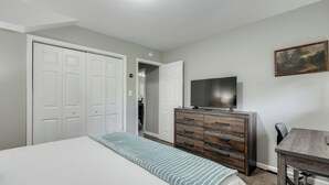 Een slaapkamer met een bed, een dressoir, een televisie en een schilderij aan de muur.