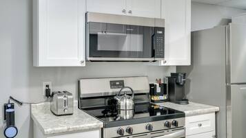 A compact kitchen with a built-in microwave, toaster, kettle, coffee maker, and stove.