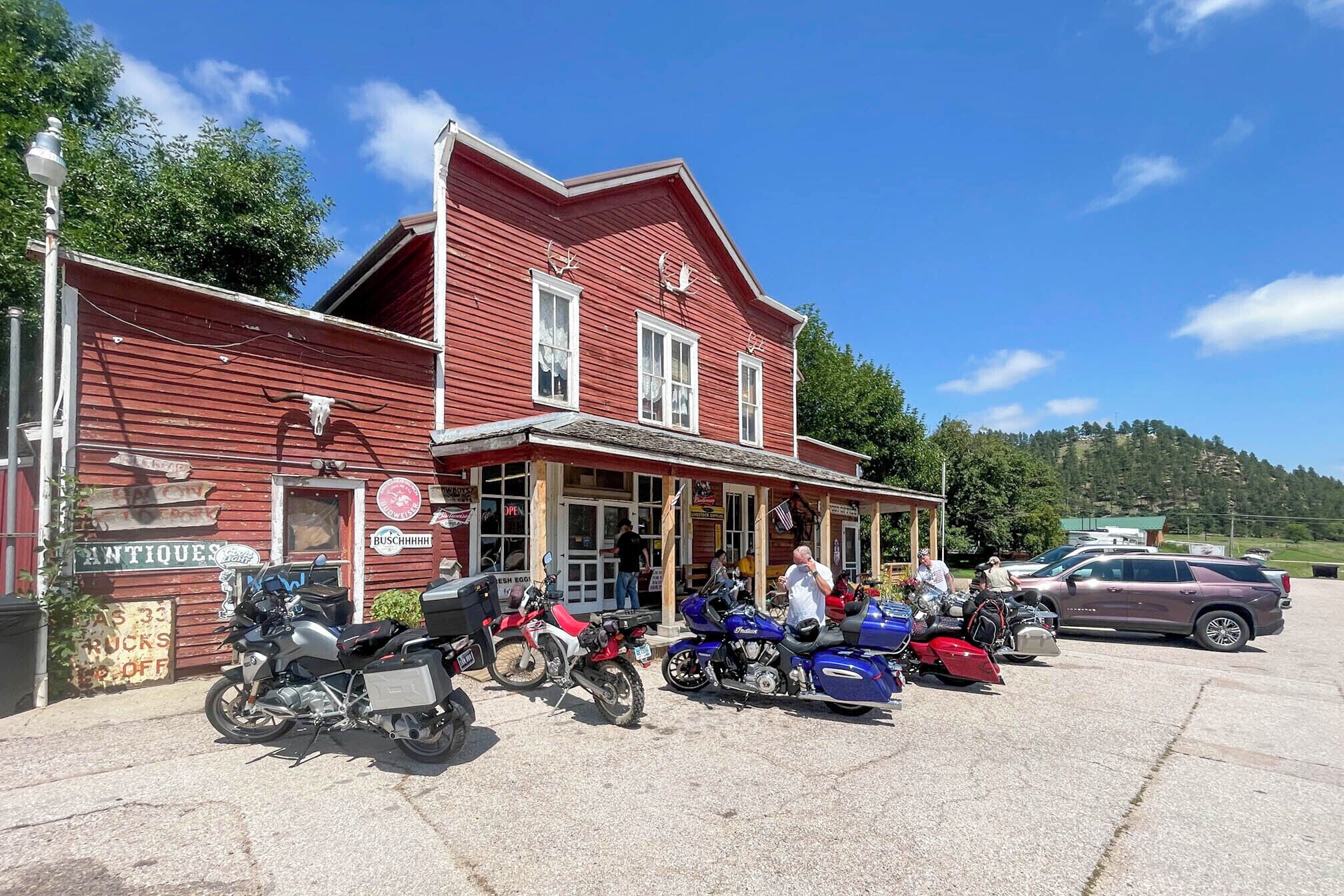 A red building with a porch, motorcycles parked in front, and a sign for 'Antiques' on the left.