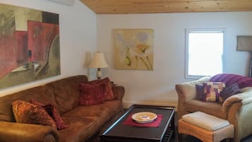 A living room with a brown sofa, a wicker chair, a coffee table, and artwork on the walls.
