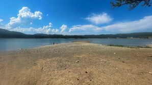 A lakeside view with a pebbly shore, calm water, and distant hills.