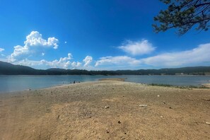 A lakeside view with a pebbly shore, calm water, and distant hills.