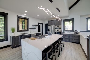 A modern kitchen with a large island, dark cabinetry, and a unique ceiling light fixture.