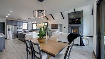 A modern kitchen with a central island, dining area with chairs, and a fireplace.