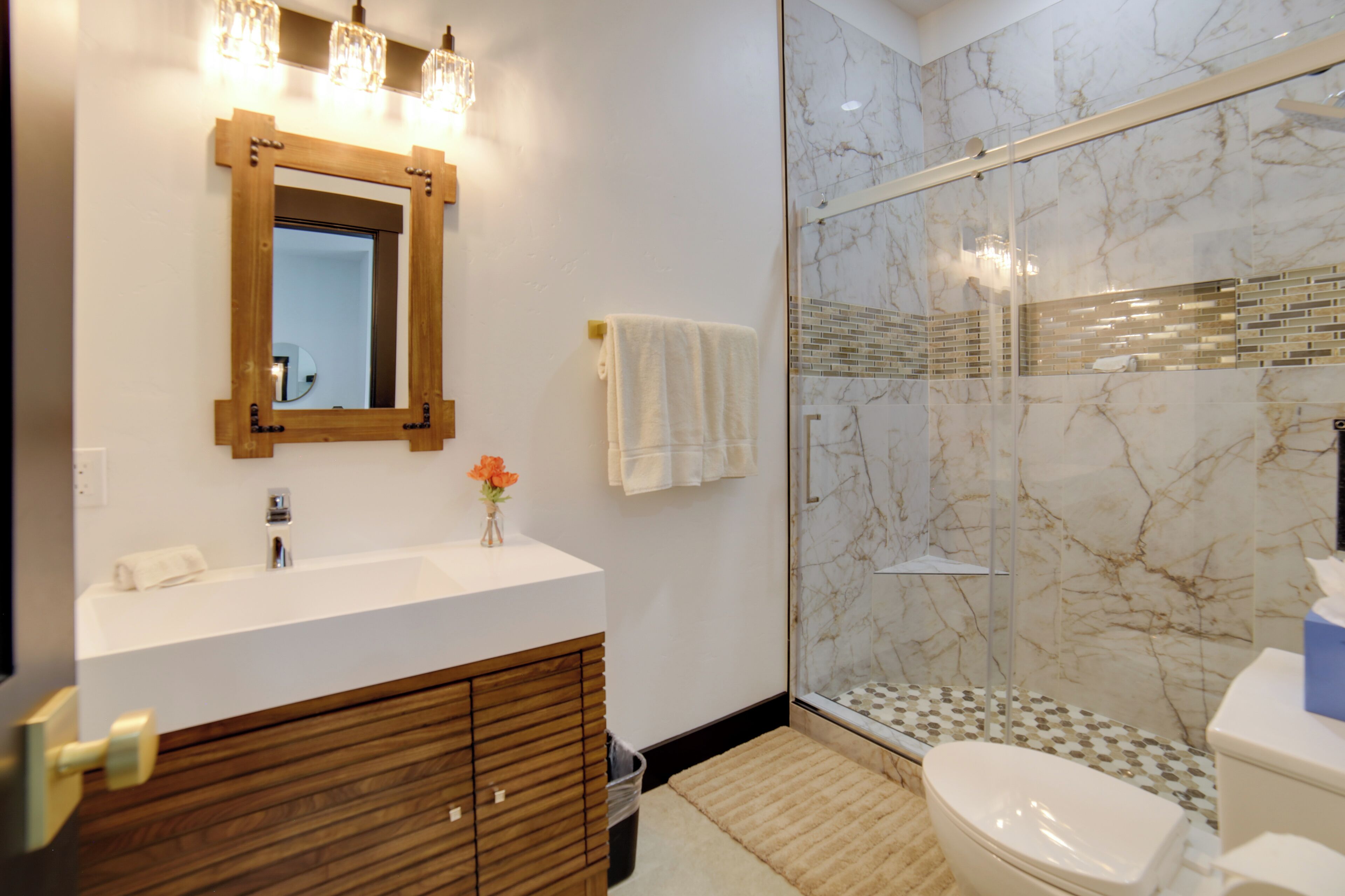 A modern bathroom with a marble shower, a wooden vanity, and a glass-enclosed shower area.