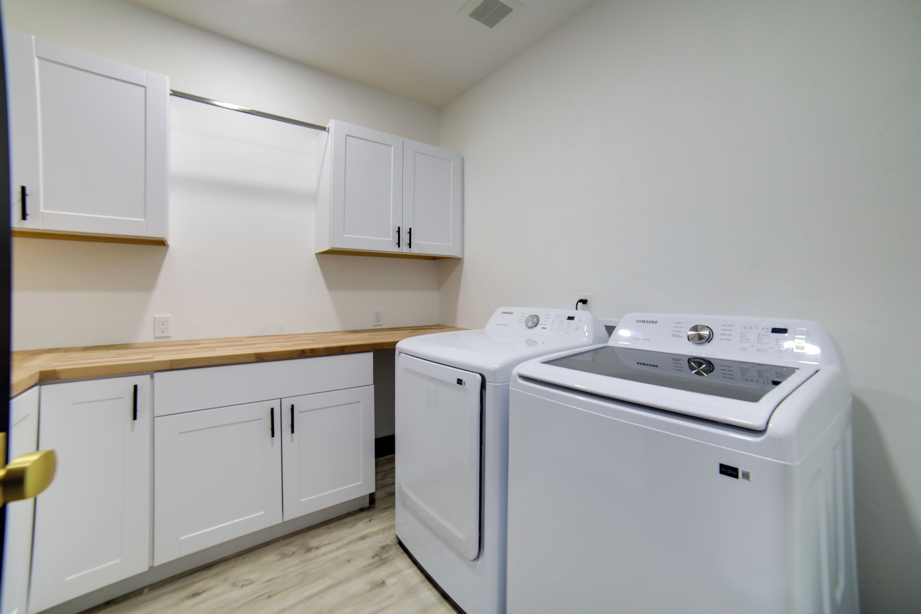 A laundry room with white cabinets, a wooden countertop, and two white washing machines.