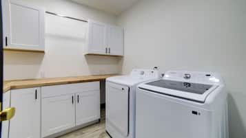 A laundry room with white cabinets, a wooden countertop, and two white washing machines.