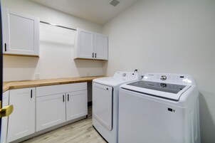 A laundry room with white cabinets, a wooden countertop, and two white washing machines.