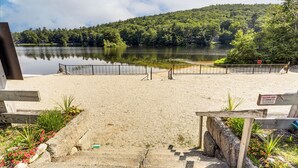 A sandy beach with a wooden fence, a sign indicating a clean air zone, and a lake with a forested hill in the background. - Lakefront Home w/ Decks & Views in Newbury (Newbury)