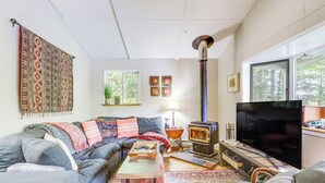 A cozy living room with a sofa, a television, a fireplace, and a large window. - Lakefront Home w/ Decks & Views in Newbury (Newbury)