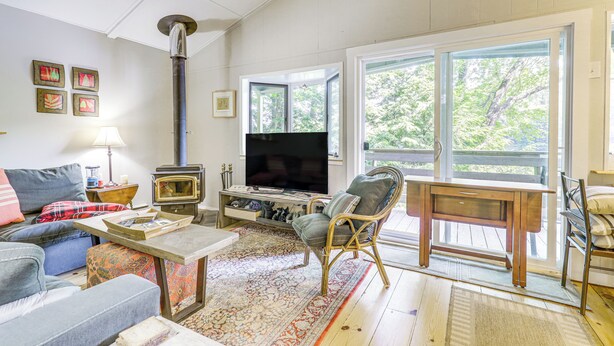 A living room with a fireplace, sofa, television, and large windows. - Lakefront Home w/ Decks & Views in Newbury (Newbury)