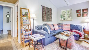 A cozy living room with a blue sofa, a coffee table, a bookshelf, and a patterned rug. - Lakefront Home w/ Decks & Views in Newbury (Newbury)