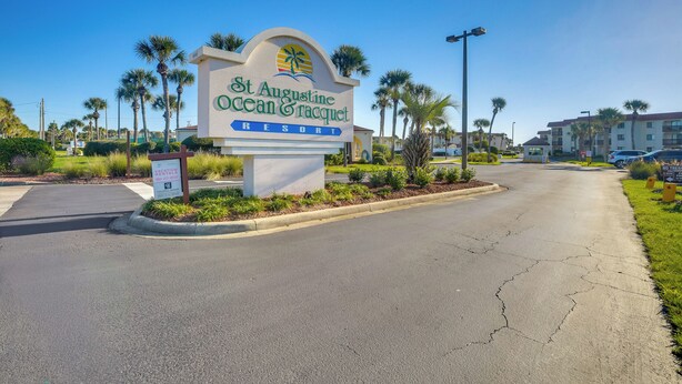 En skylt för St. Augustine Ocean & Racquet Resort, med en tydlig väg och palmer i bakgrunden.