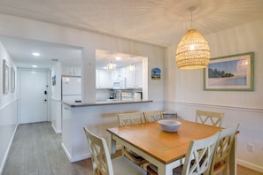 A dining area with a wooden table and chairs, a kitchen with white cabinets, and a hanging light fixture. - Walk to Beach! Set of 2 St Augustine Condos (St. Augustine)