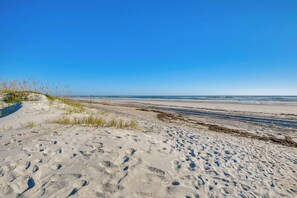 Ein sandiger Strand mit Fußabdrücken und vereinzelter Vegetation.