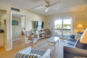 A spacious living room with a ceiling fan, a television, a dining area with wicker chairs, a sofa, and a balcony with a view. - Walk to Beach! Set of 2 St Augustine Condos (St. Augustine)