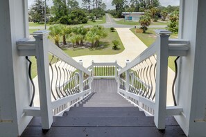 A staircase leading to a covered outdoor area with a view of a residential street and greenery. - Waterfront Family Home w/ Views in Carrabelle (Carrabelle)