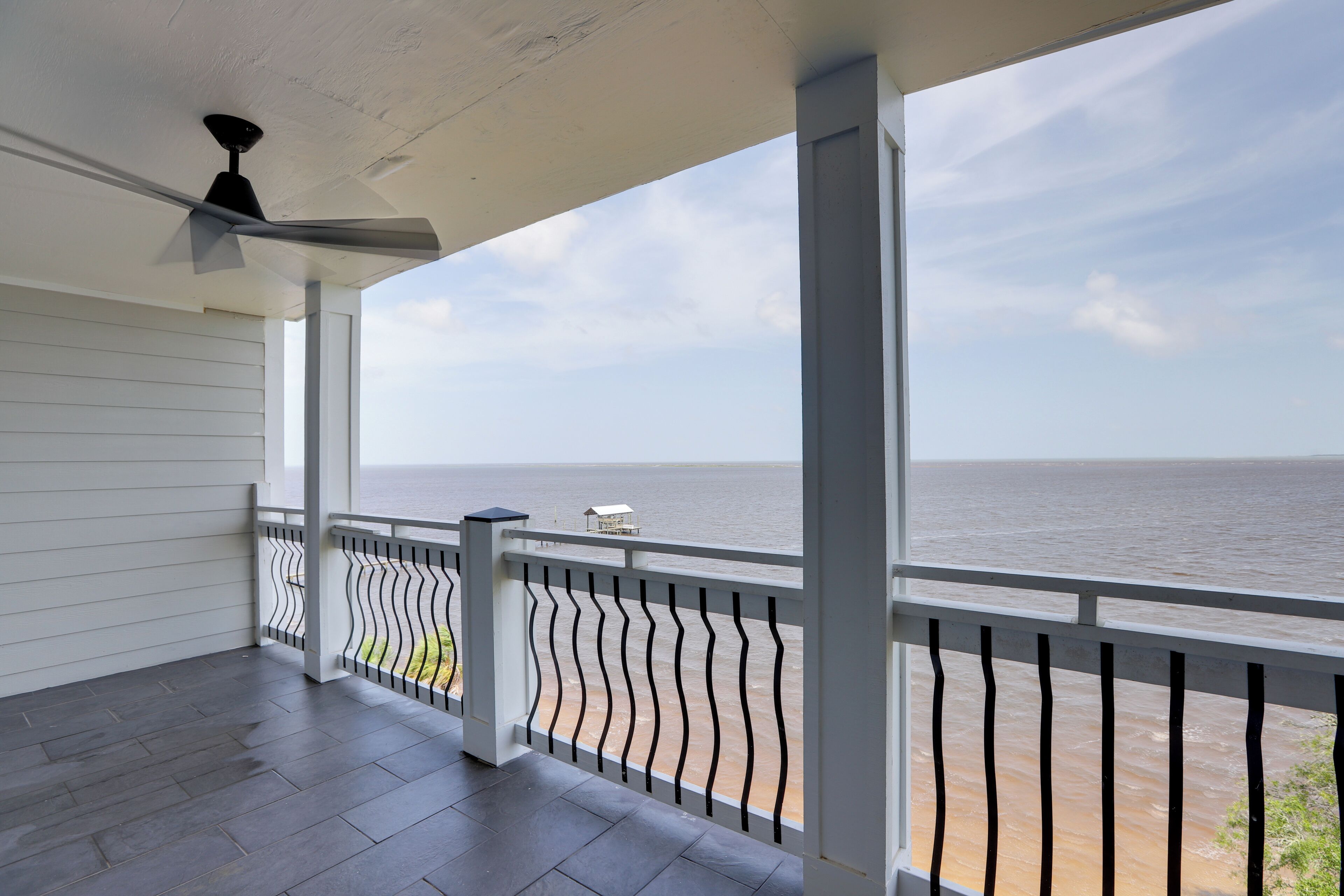 A covered balcony with a view of the sea, a ceiling fan, and a railing.