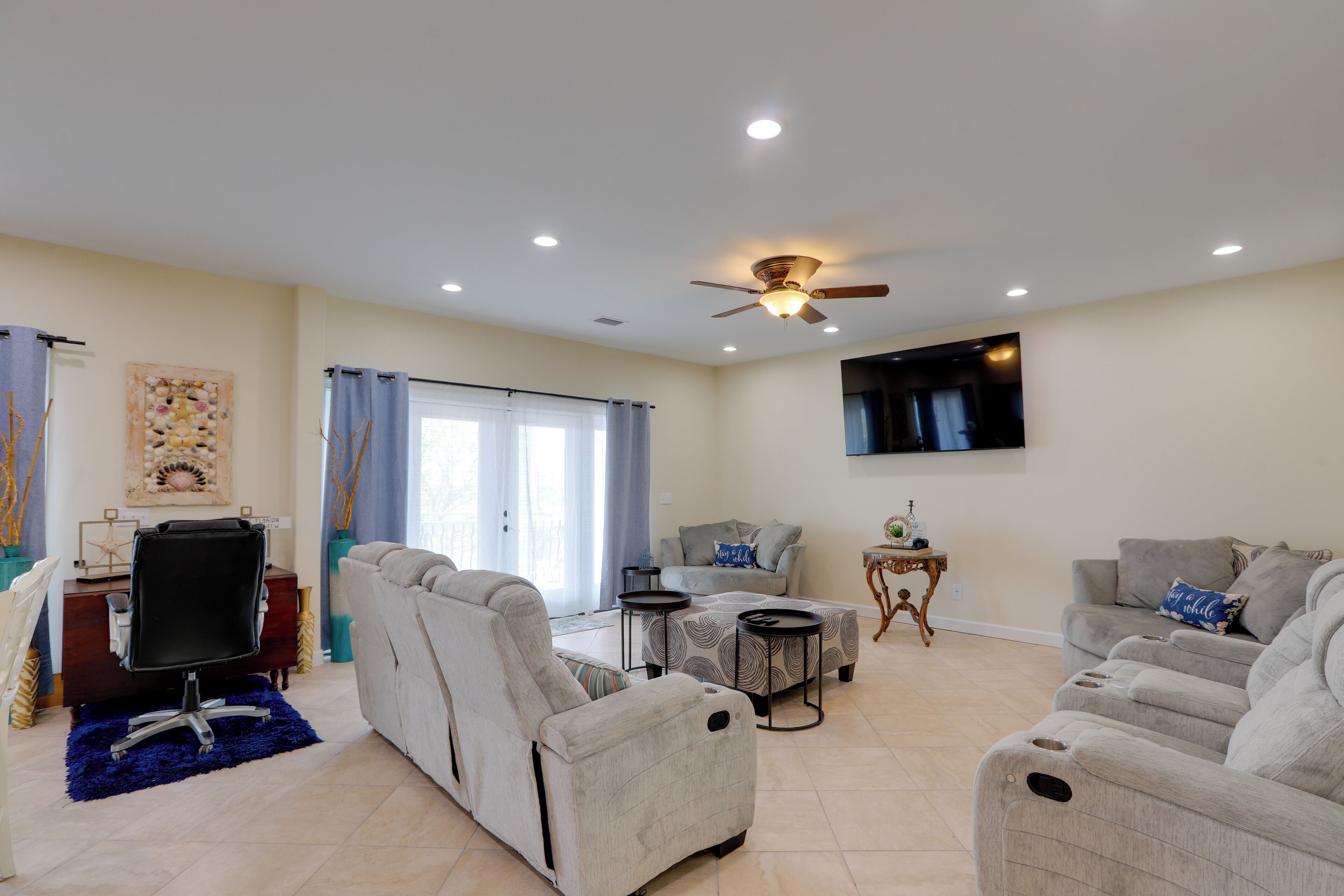 A living room with a ceiling fan, a flat-screen TV, and a sofa set.