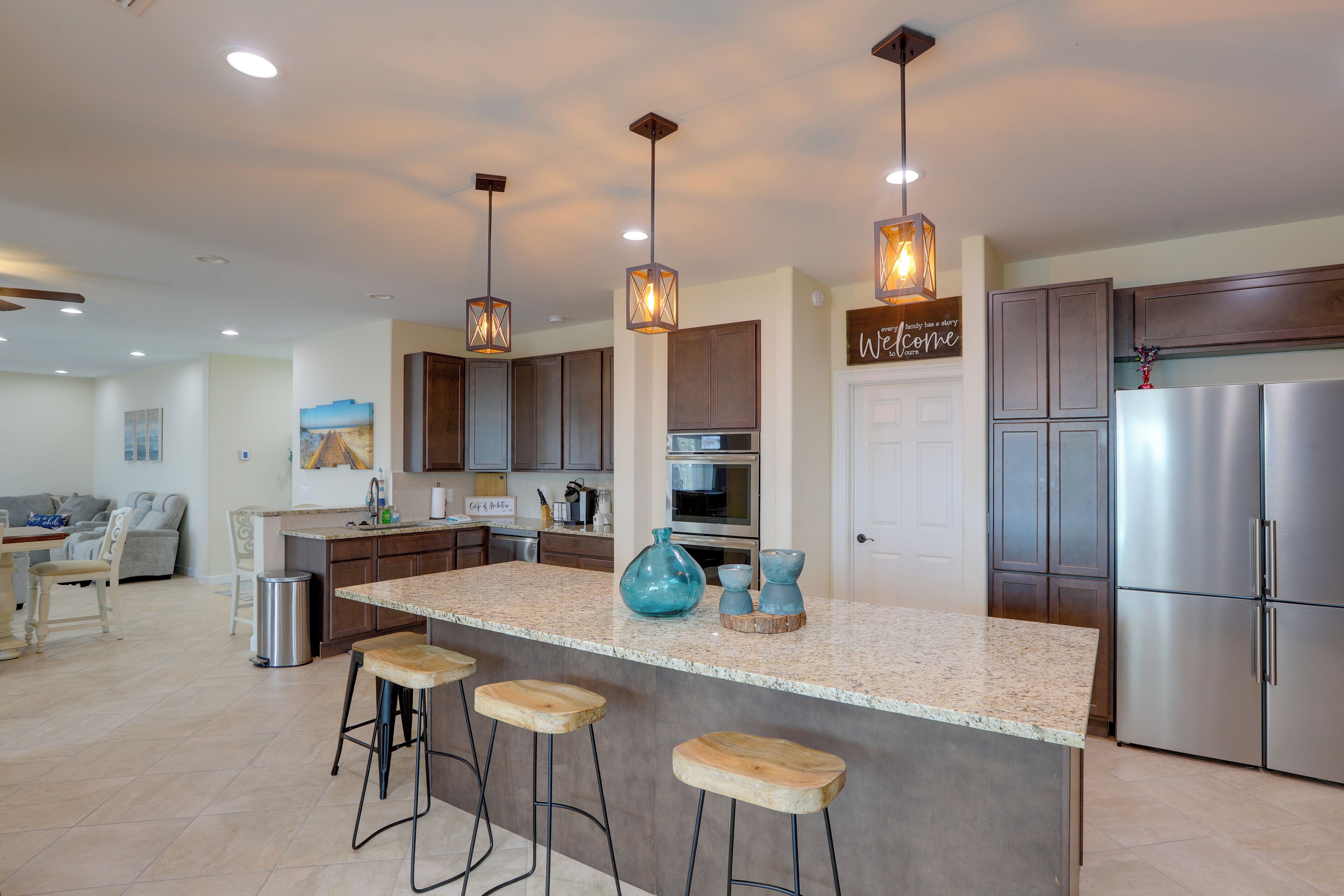 A modern kitchen with a central island, bar stools, stainless steel appliances, and pendant lighting.