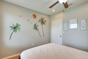 A bedroom with a bed, a ceiling fan, a door, and wall art including palm trees and birds. - Pet-friendly Cape Coral Home w/ Pool & Hot Tub (Cape Coral)