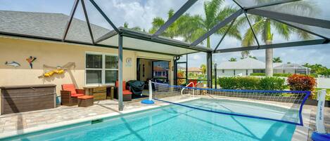 A swimming pool with a safety net, surrounded by lounge chairs and a covered patio area.