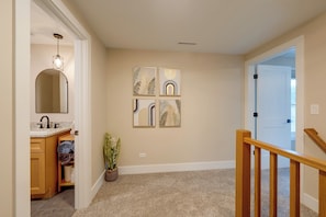 A hallway with a wooden staircase, a bathroom with a sink and towel rack, and four framed wall art pieces. - Walk to Beach! Mccullom Lake Family Getaway (McHenry)
