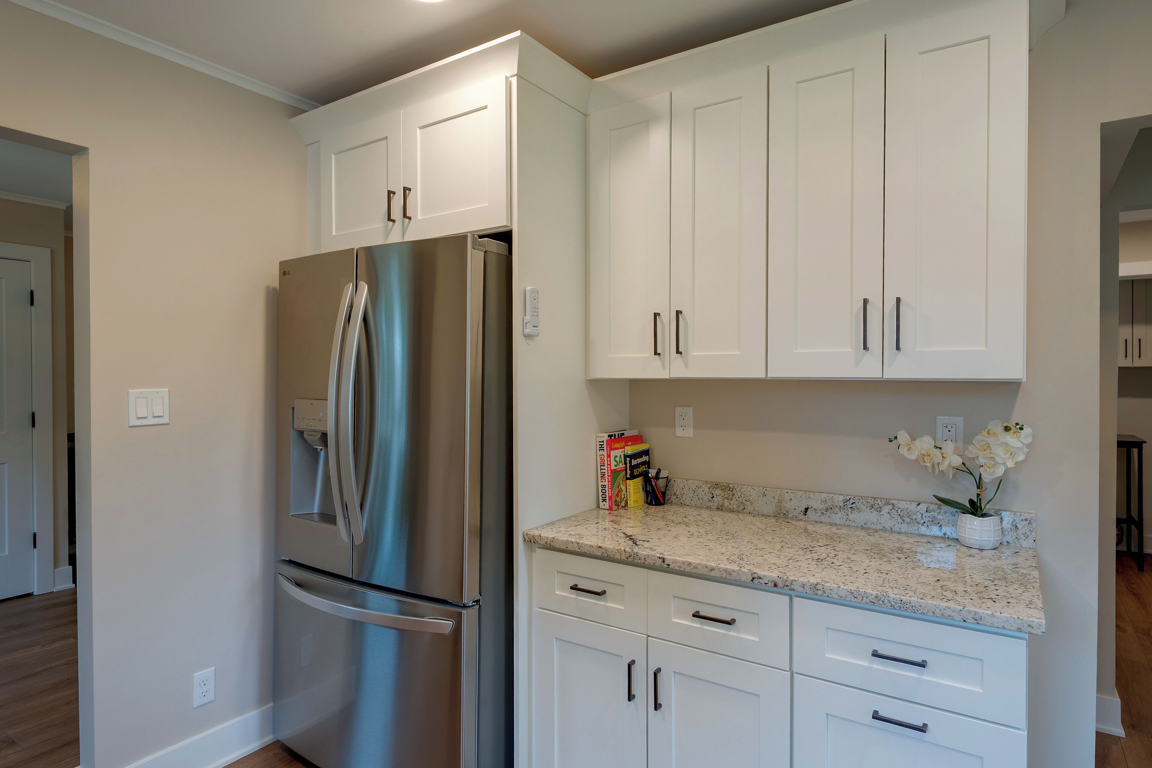 Una cocina con gabinetes blancos, un refrigerador de acero inoxidable y una encimera de granito.