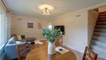 Una sala de estar moderna con un sofá, una mesa de comedor con sillas, un televisor y una escalera.