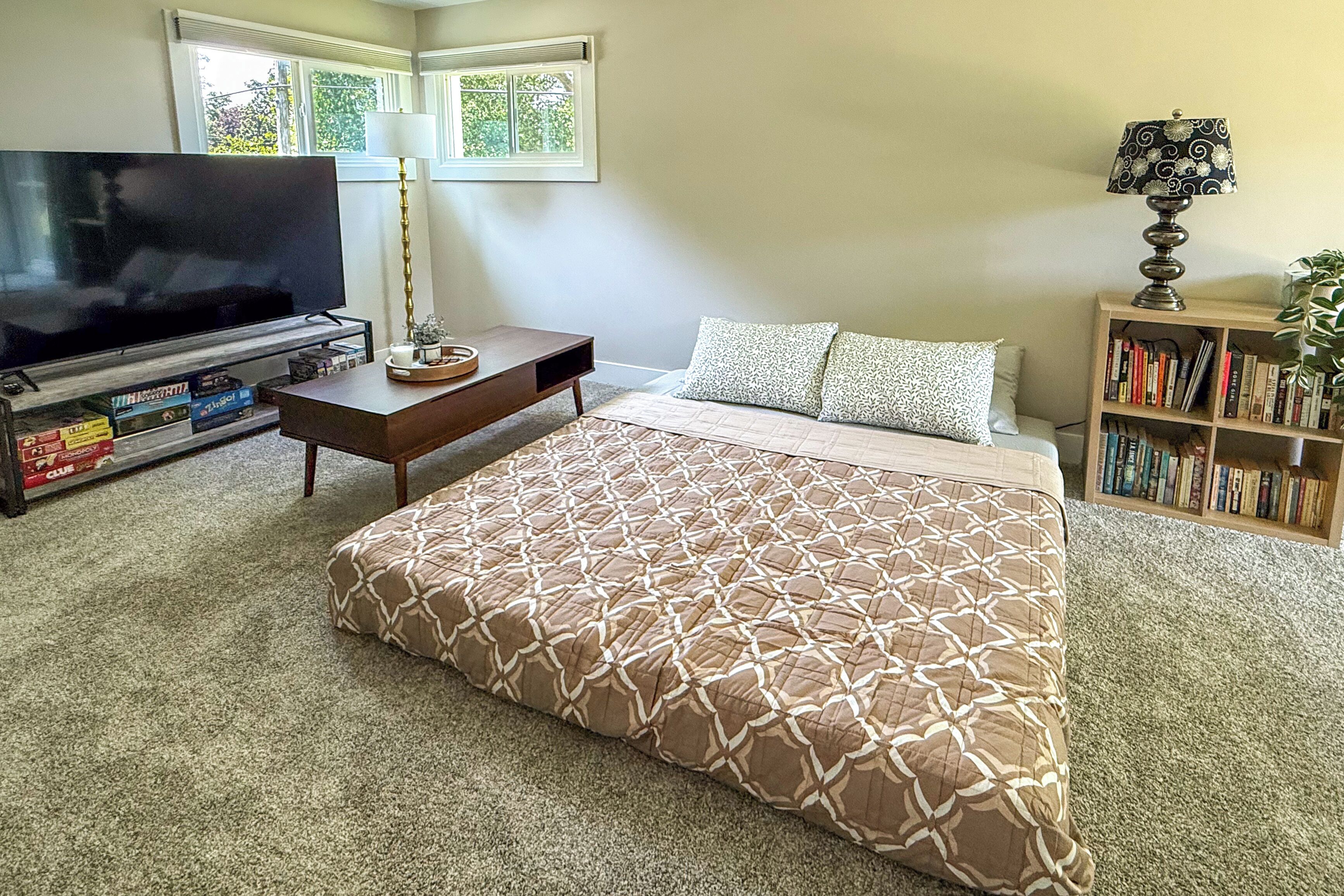 A bedroom with a large bed, a TV, a bookshelf, and a window with a view.