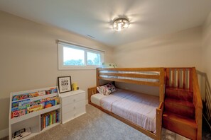 A child's bedroom with bunk beds, a bookshelf with books, a window, and a ceiling light fixture.