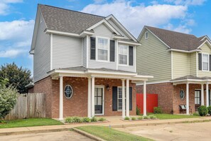 A two-story residential building with a brick facade, a front porch, and a red garage door.