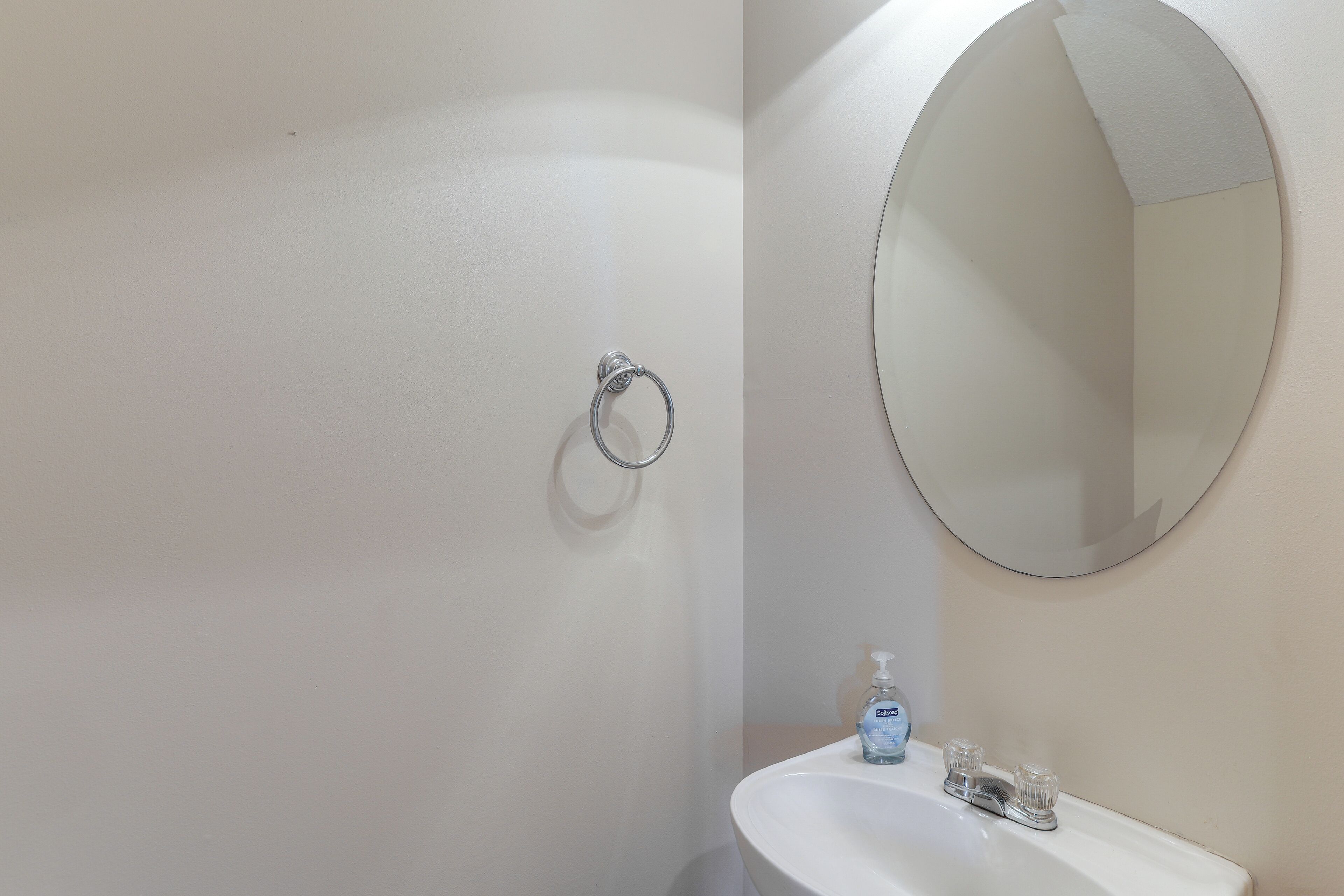 Une salle de bain avec un lavabo blanc, un miroir rond et un porte-serviettes fixé au mur.