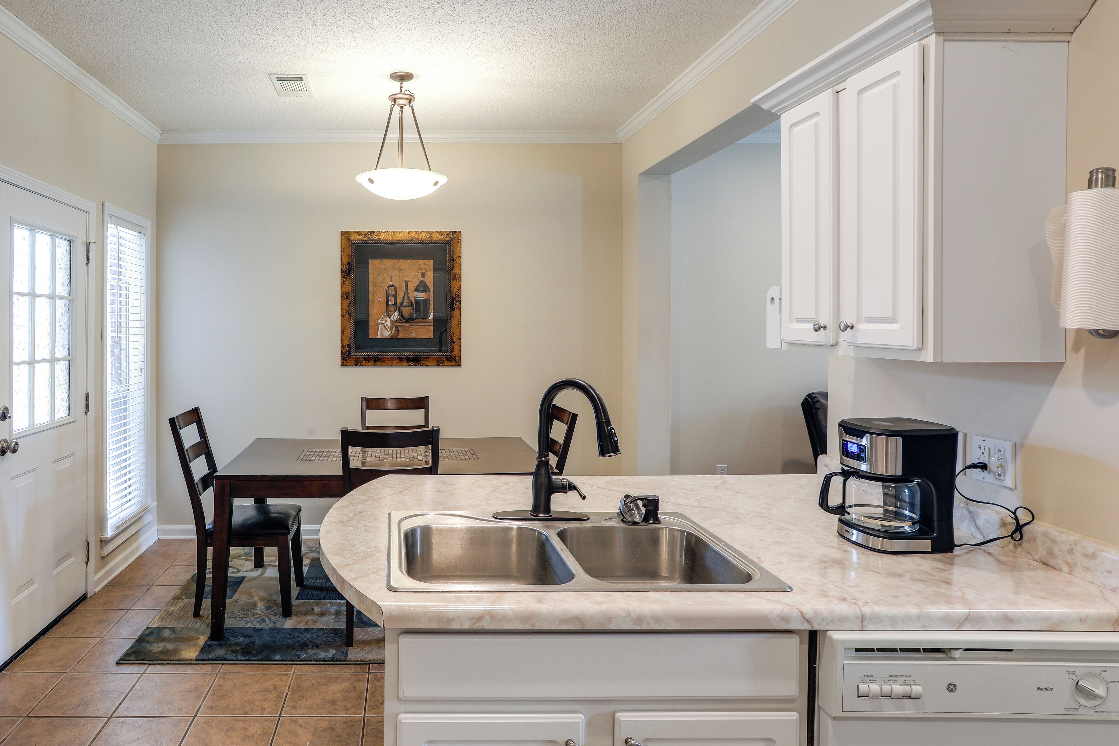 A kitchen with a double sink, a coffee maker, and a dining area with a table and chairs.