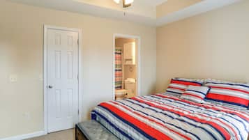 A bedroom with a bed, a door, a ceiling fan, and a bathroom visible through an open door.