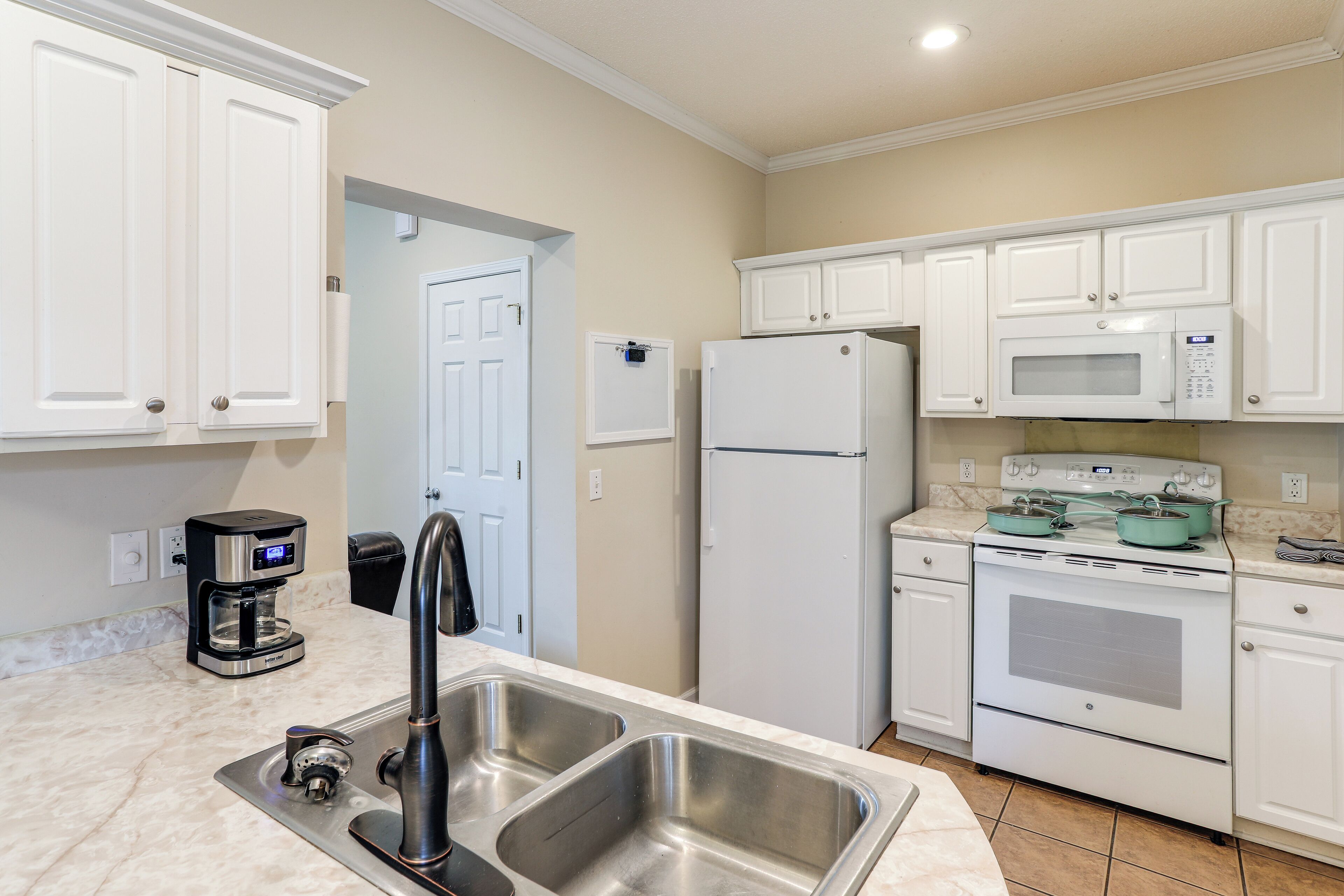 A kitchen with white cabinets, a stainless steel sink, a coffee maker, a refrigerator, a microwave, and an oven.