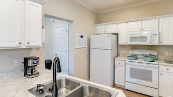 A kitchen with white cabinets, a stainless steel sink, a coffee maker, a refrigerator, a microwave, and an oven.