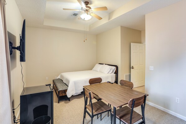 A compact room with a bed, a table, and a ceiling fan.