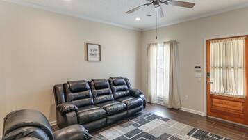 A living room with a leather sofa, a ceiling fan, and a door with curtains.