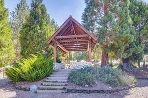 A wooden gazebo with a stone bench, surrounded by trees and a gravel path.
