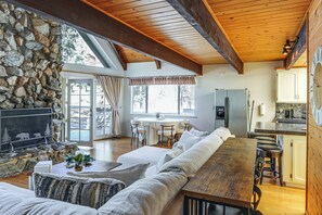 A cozy living room with a stone wall, a fireplace, and a dining area with a table and chairs. - Hike, Swim & Relax: Pine Mountain Club Escape! (Pine Mountain Club)