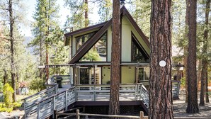 Mökki, jossa on puinen terassi, portaikko ja näkymä ympäröivään metsään.