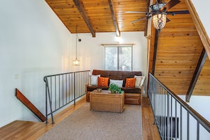 Un interior de madera con una escalera, una zona de estar con cojines y una lámpara colgante.