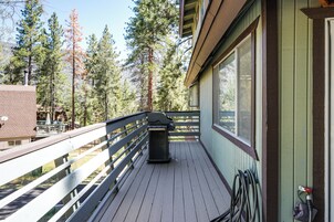 Una terraza de madera con barandilla, una parrilla y una ventana con vista a un bosque.