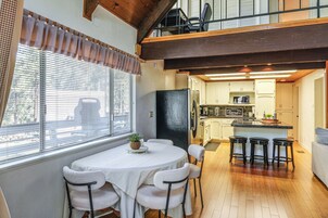 Un comedor con una mesa y sillas, una cocina al fondo y vistas por la ventana.