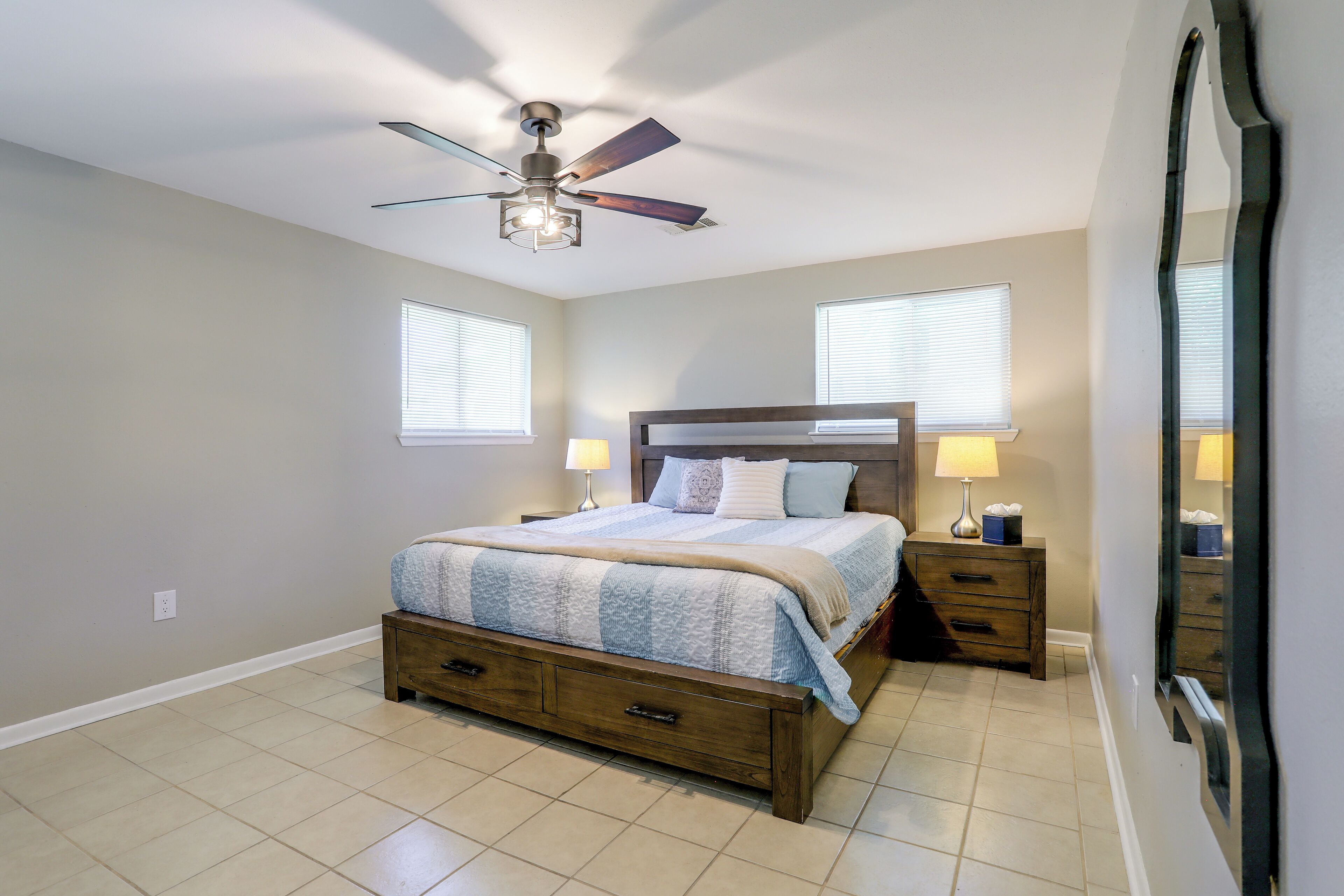 Quarto com cama, mesas de cabeceira, ventilador de teto e um espelho grande.