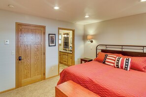 A bedroom with a wooden door, a mirror, a bedside table, and a bed with a red quilt.