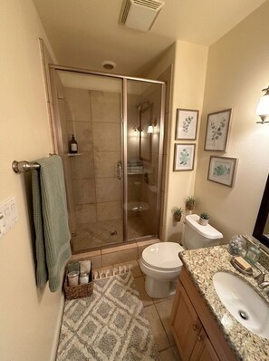 A bathroom with a glass-enclosed shower, a toilet, a sink, and framed artwork on the wall. - Snowbird Desert Condo - Tennis Garden, Golf, 2BR/2BA (La Quinta)