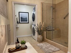 A bathroom with a glass shower enclosure, a washing machine, and a drying rack. - Snowbird Desert Condo - Tennis Garden, Golf, 2BR/2BA (La Quinta)